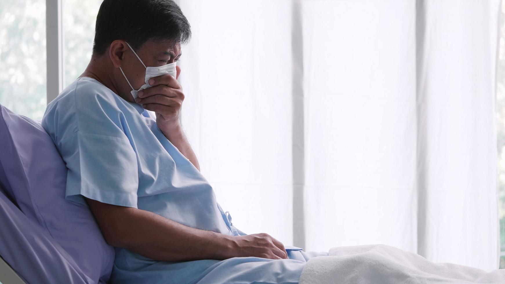 Asian old man is hospitalized with COVID-19. Old male patient wearing a medical mask sits on the patient's bed. photo