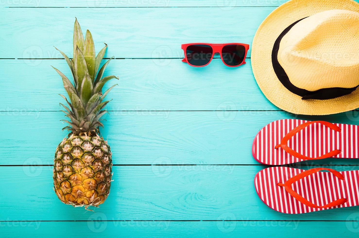 Flip flops, pineapple, hat and sunglasses. Summer accessories for modern woman on her vacation. Top view. Blue wooden background with copy space. photo