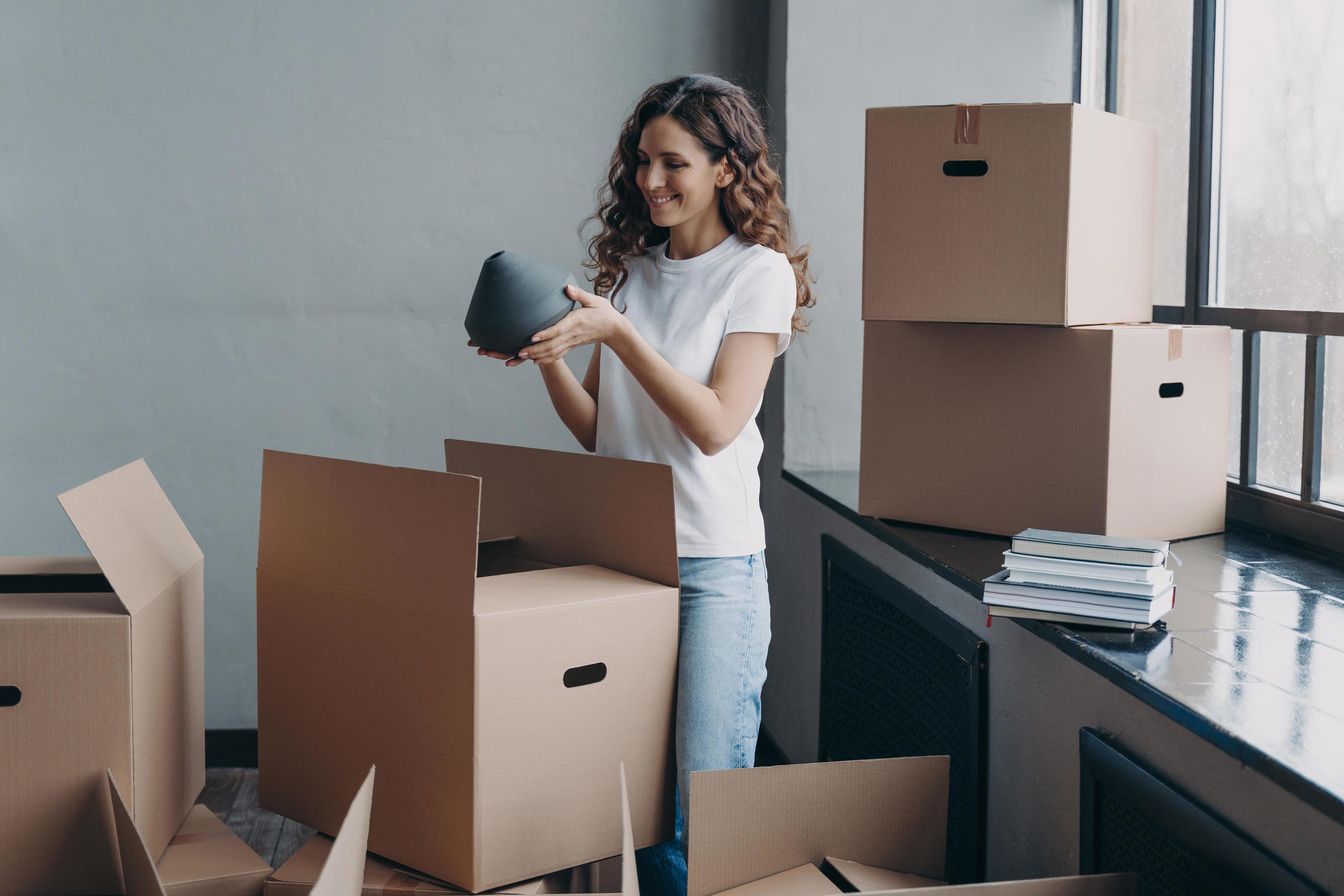 Happy girl unpacking cardboard boxes and taking the vase. European