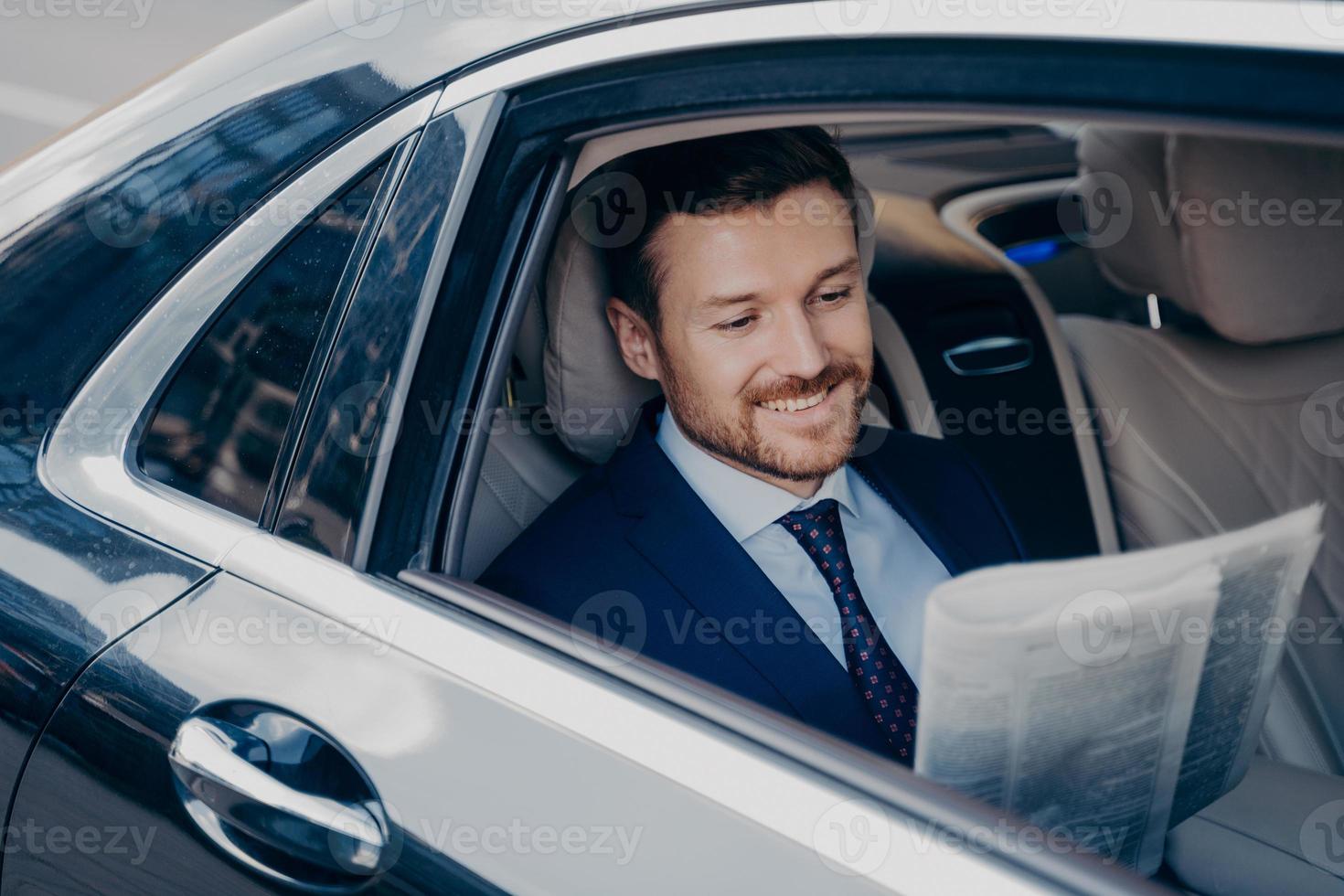 Handsome young banker in smart formal tuxedo suit reads newspaper in luxury auto photo