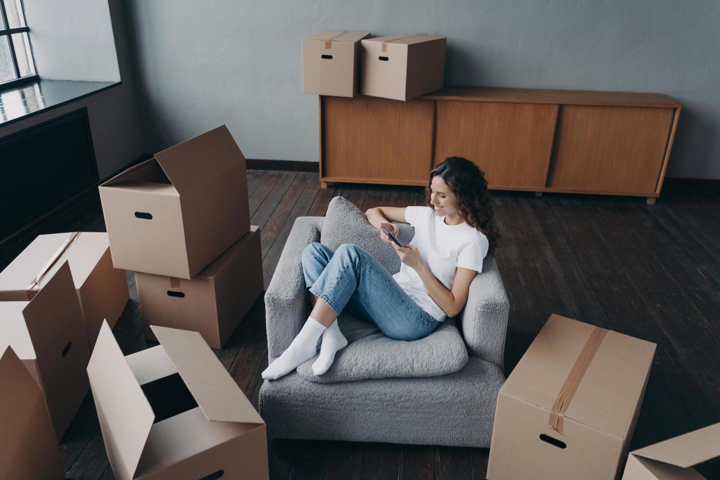 Girl having rest in new apartment and clicks phone. Independent spanish woman is moving. photo