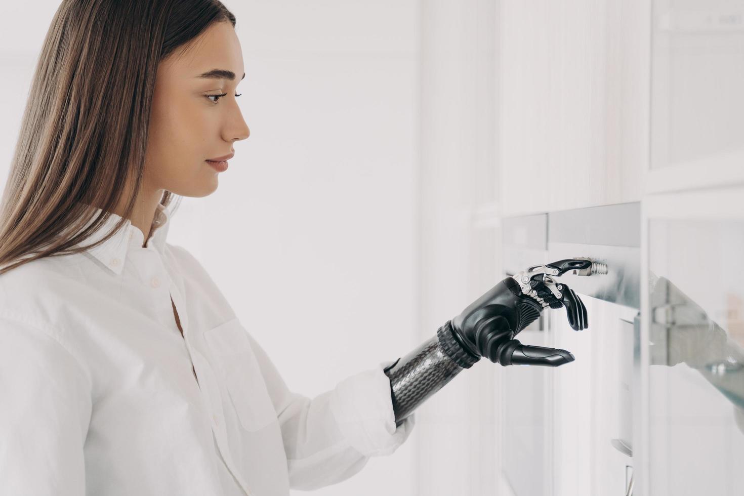European handicapped woman is cooking. Robotic cyber hand is switching oven on at kitchen. photo