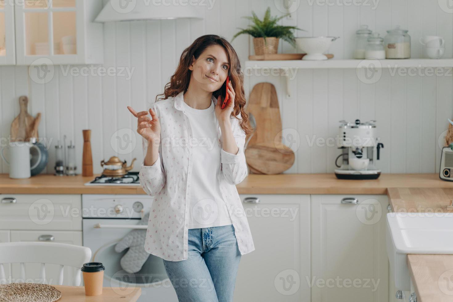 joven hispana hablando por teléfono. ama de casa relajada en su elegante cocina en casa. foto