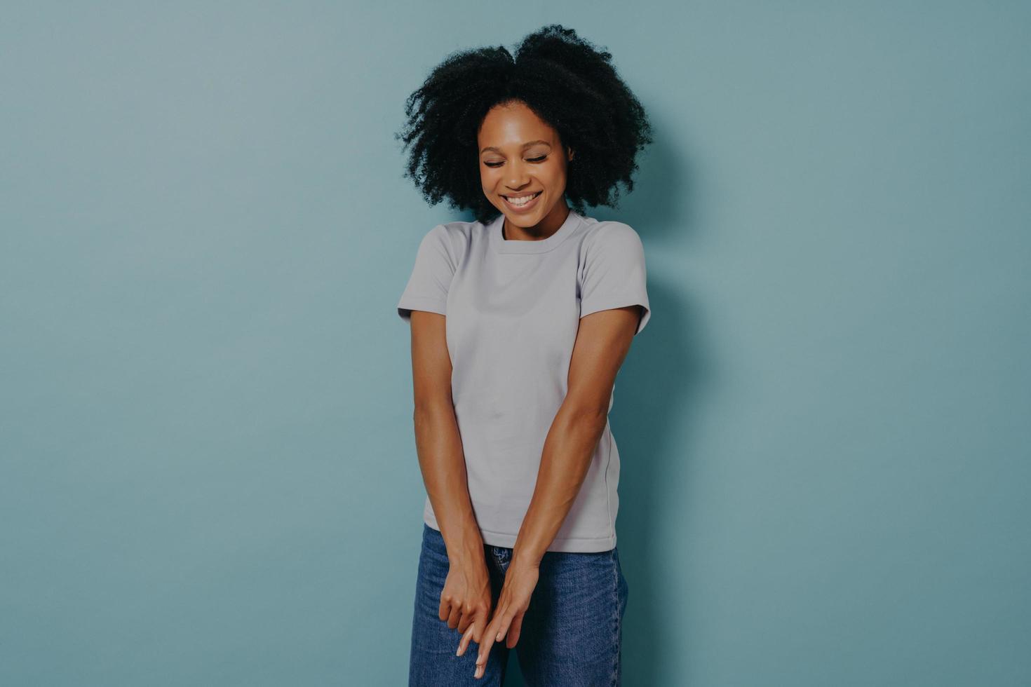 Young african lady looking down with with shy timid face expression, isolated over blue background photo