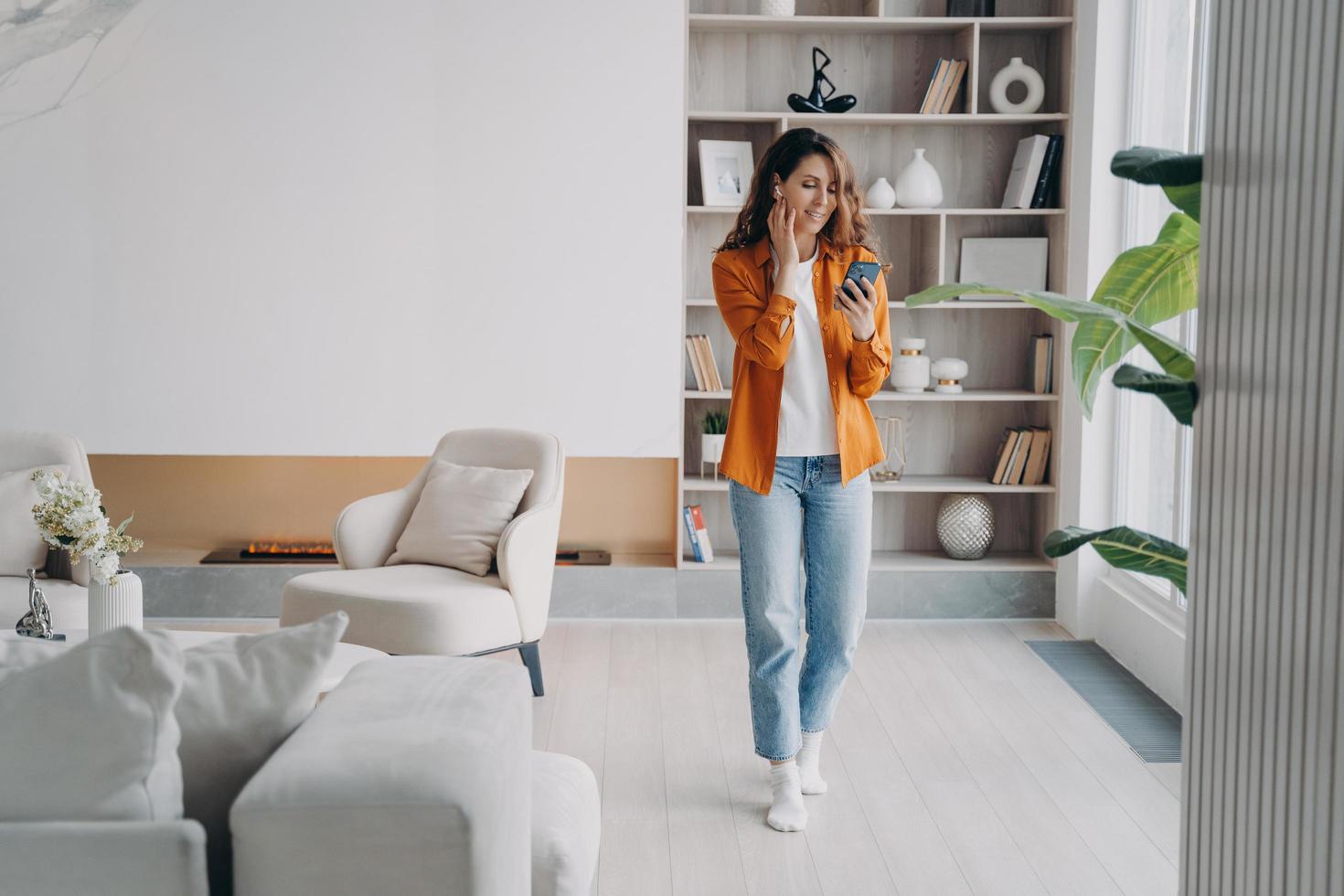 una chica europea feliz con auriculares tiene una llamada telefónica en casa. Uso de auriculares inalámbricos. foto