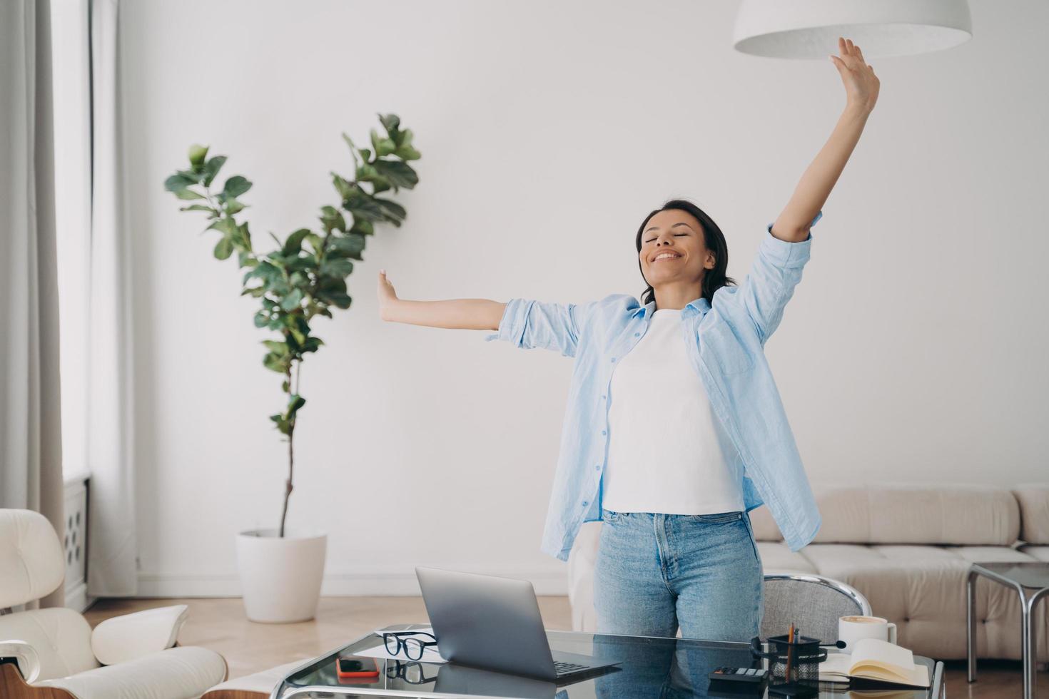 Happy female stands stretching at workplace, relaxing enjoying break after successful work at laptop photo