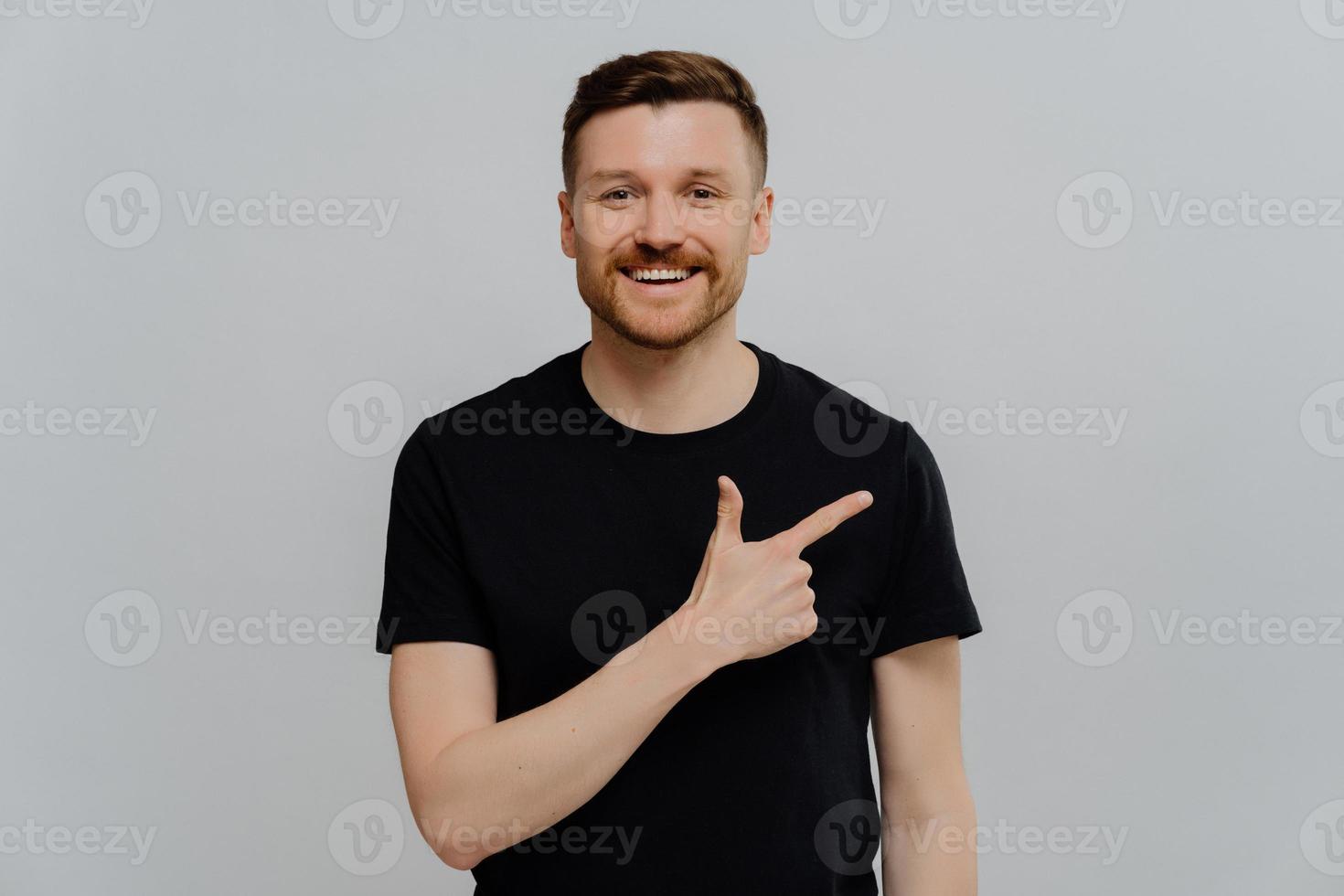 Young positive man pointing at upper right corner with pleased face expression photo