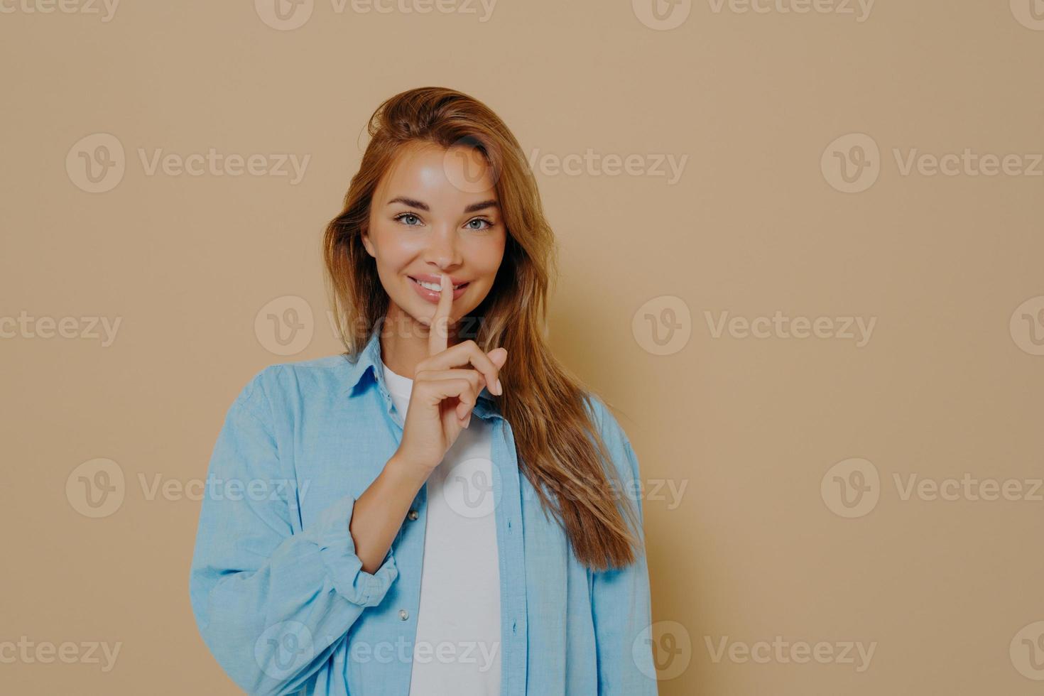 mujer emocionada mostrando gesto de silencio sobre fondo beige foto