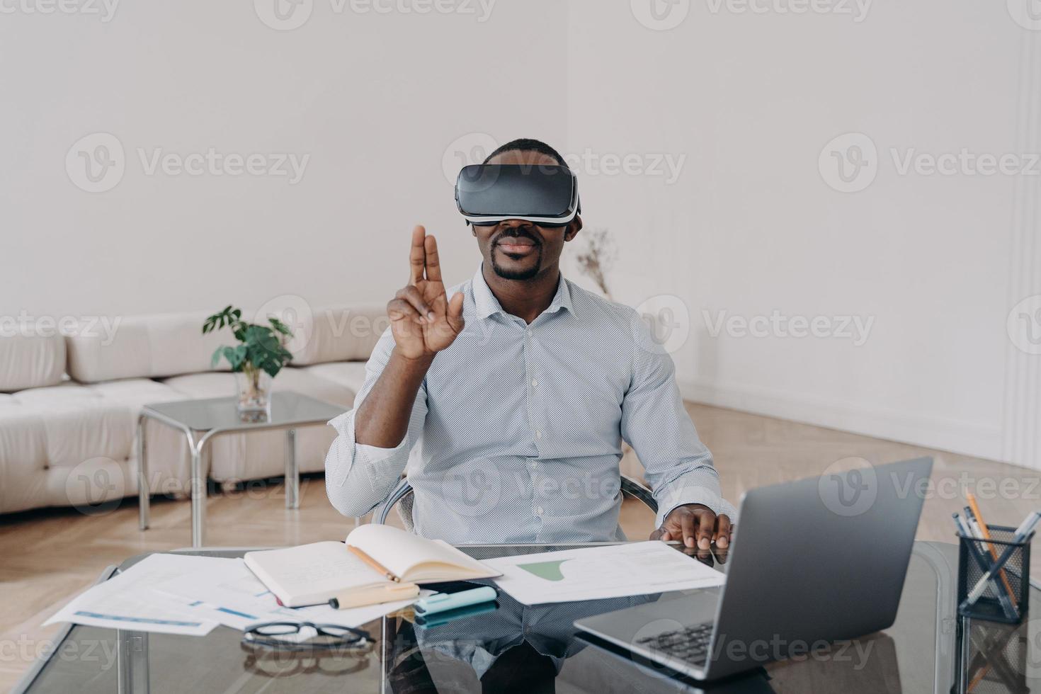 African american businessman using virtual reality glasses working at laptop. Hightech, e-business photo