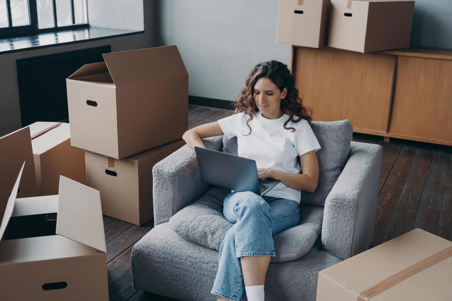 Happy hispanic woman renting apartment online. Homeowner is sitting in armchair with pc. photo