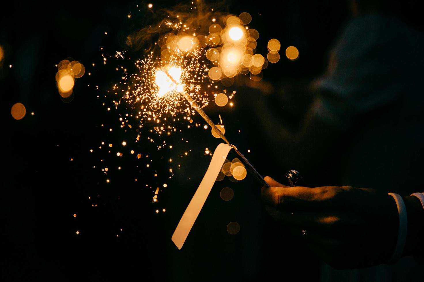 bengala festiva brillante en la mano. chispa ardiente en la oscuridad. persona irreconocible sosteniendo brillantes fuegos artificiales de mano de vacaciones, llama de fuego brillante. fuego de bengala contra fondo negro foto