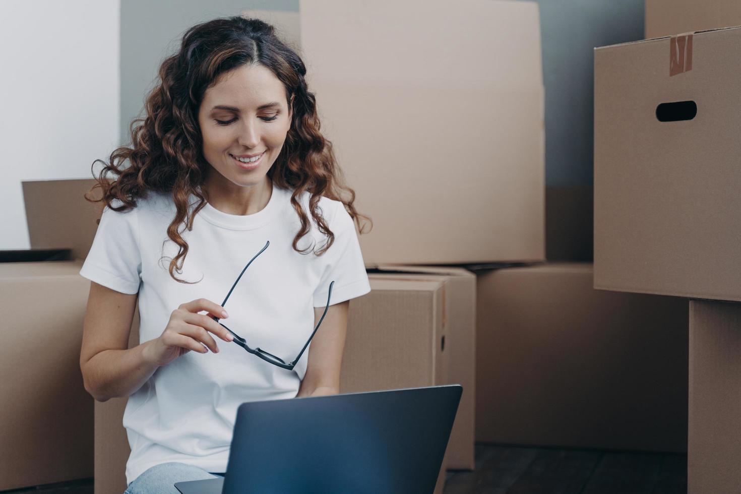 la chica española está sentada en el suelo con un portátil antes de salir del apartamento. trabajo a distancia y freelance. foto