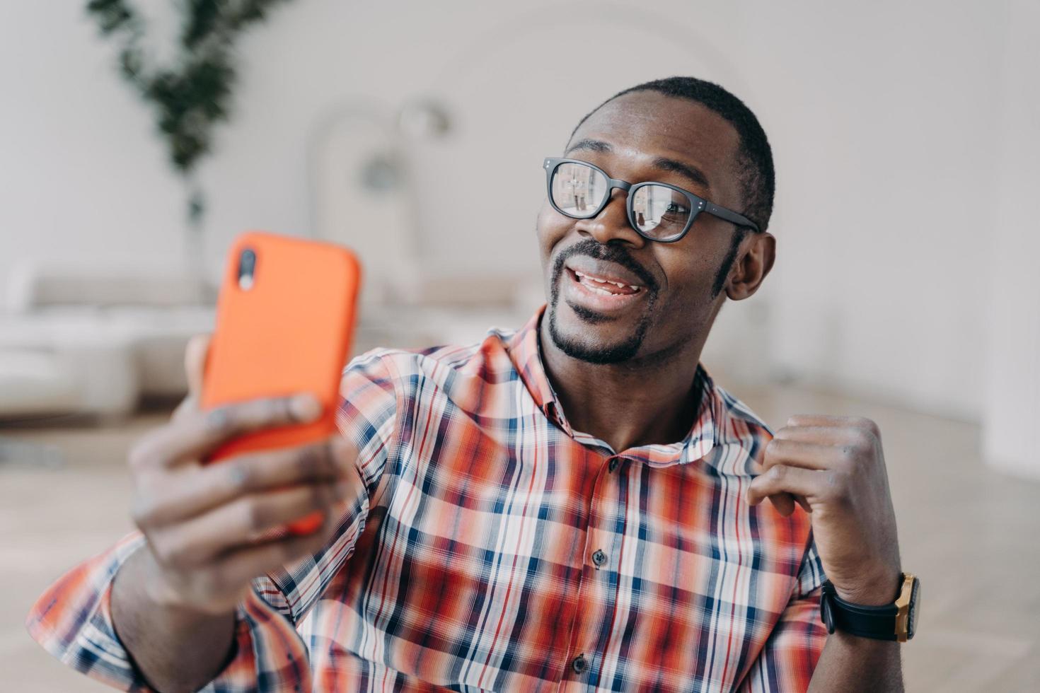 Positive afro man has video call on smartphone. Guy stays home and has conversation online. photo