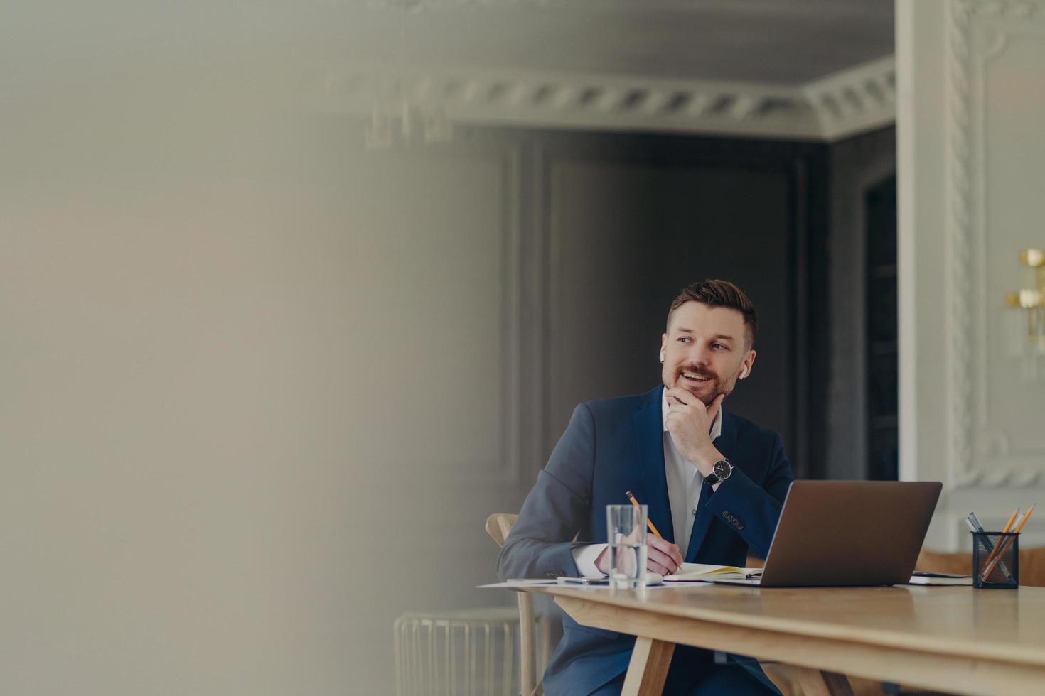 Excited businessman working in front of laptop, looking aside while making notes photo