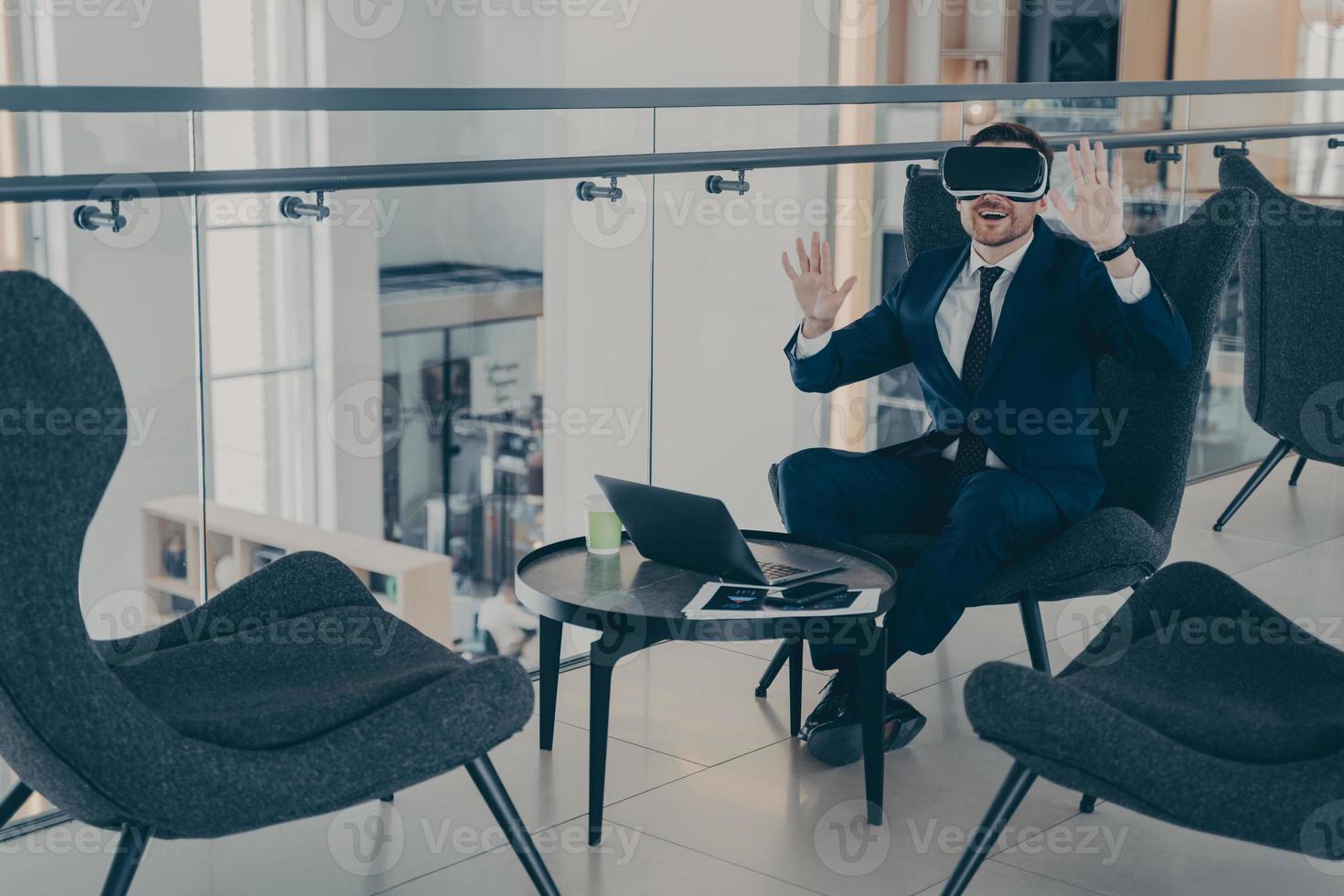 Businessman sitting in reception area of office centre during his coffee break in VR headset photo