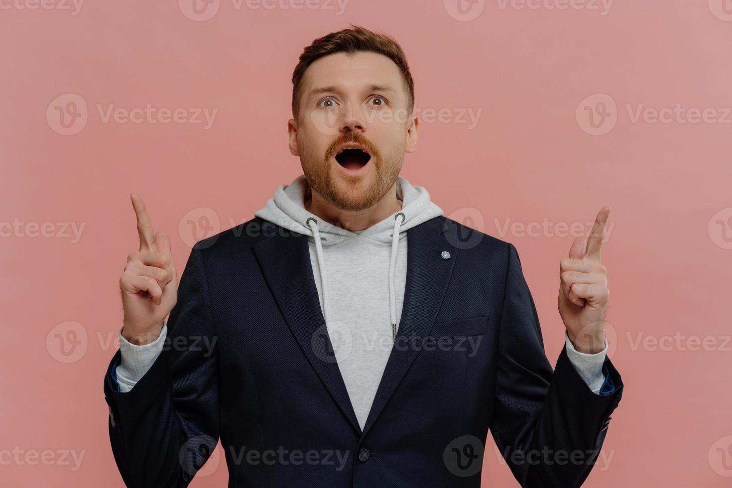 Shocked ginger man pointing up with index fingers with wow face expression photo