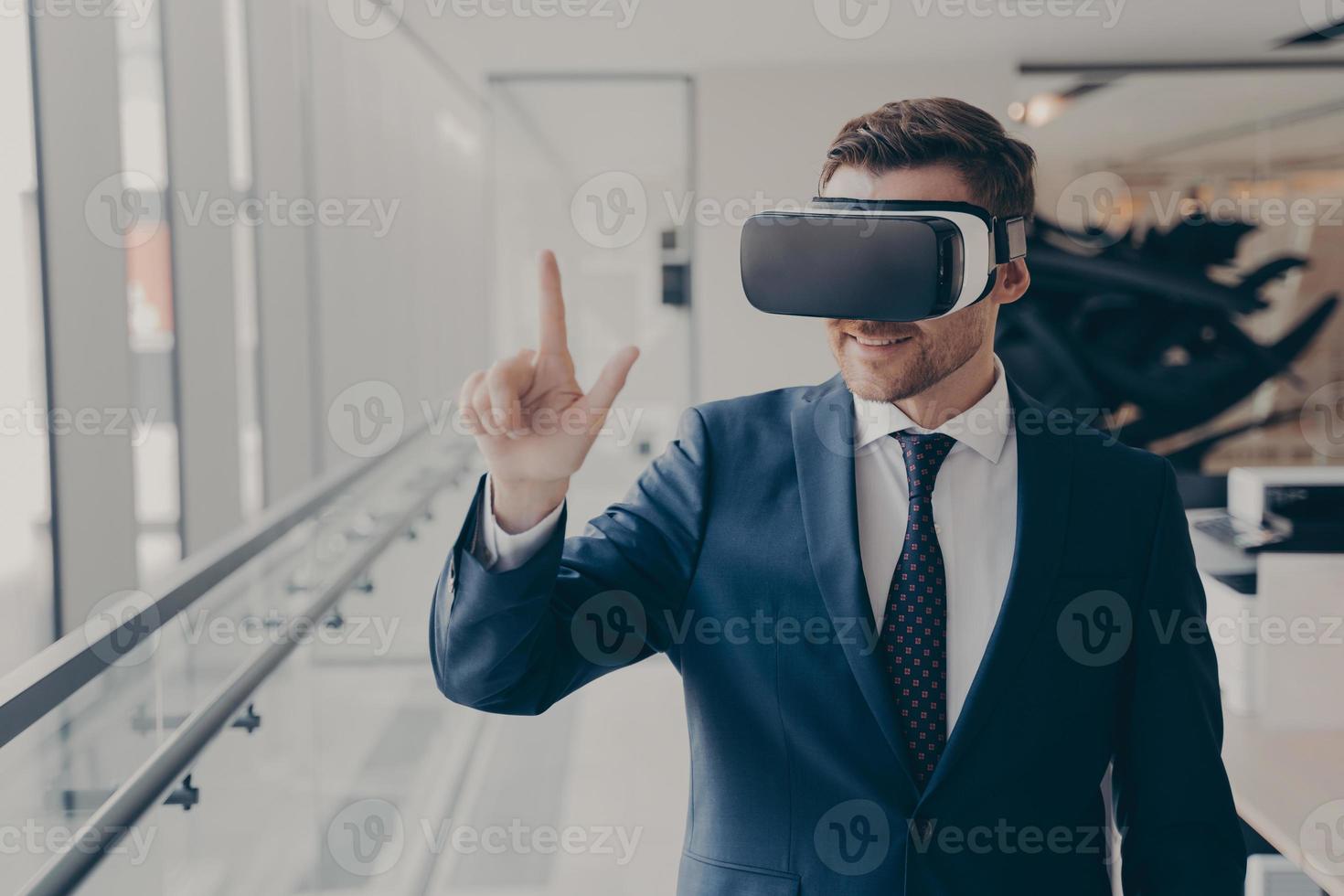 Smiling business professional in suit wearing VR headset on head using virtual reality at workplace photo