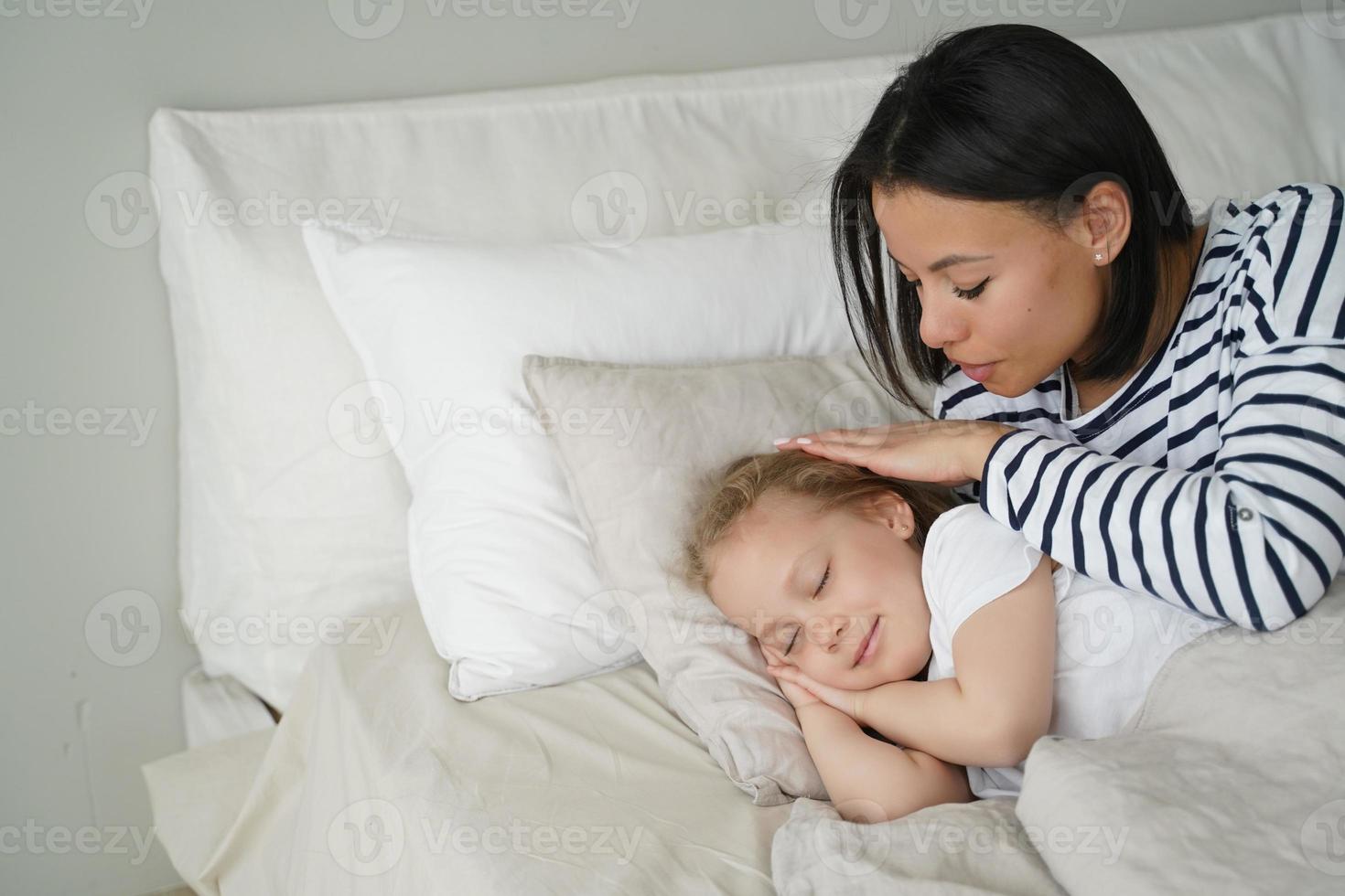 Mother puts daughter to bed, lying on soft pillow. Daytime nap, healthy sleep in children, childcare photo