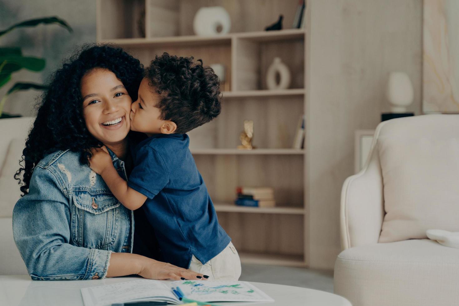 Portrait of afro american cute boy in blue polo tshirt hugging mother and kissing her in cheek photo