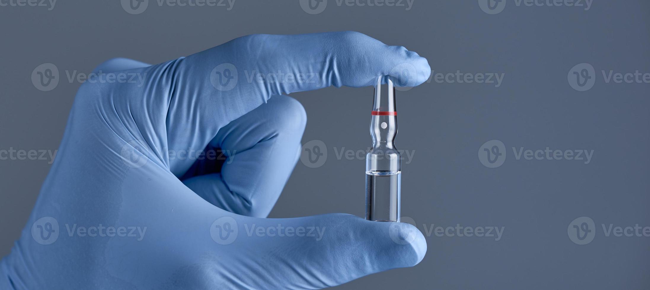 Hand in medical blue glove holding ampoule on a grey background. Concept of medical help. photo