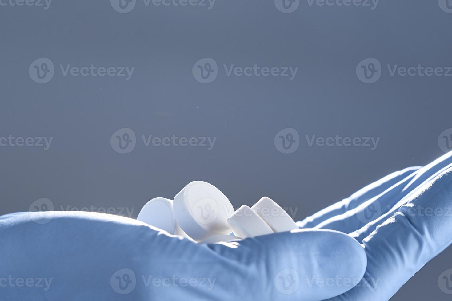 foto con espacio de copia. las tabletas blancas se sostienen con una mano en un guante médico aislado en un fondo gris.