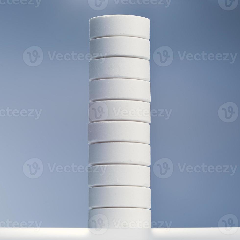 Stack of white capsules stands on a white table isolated on gray background. photo