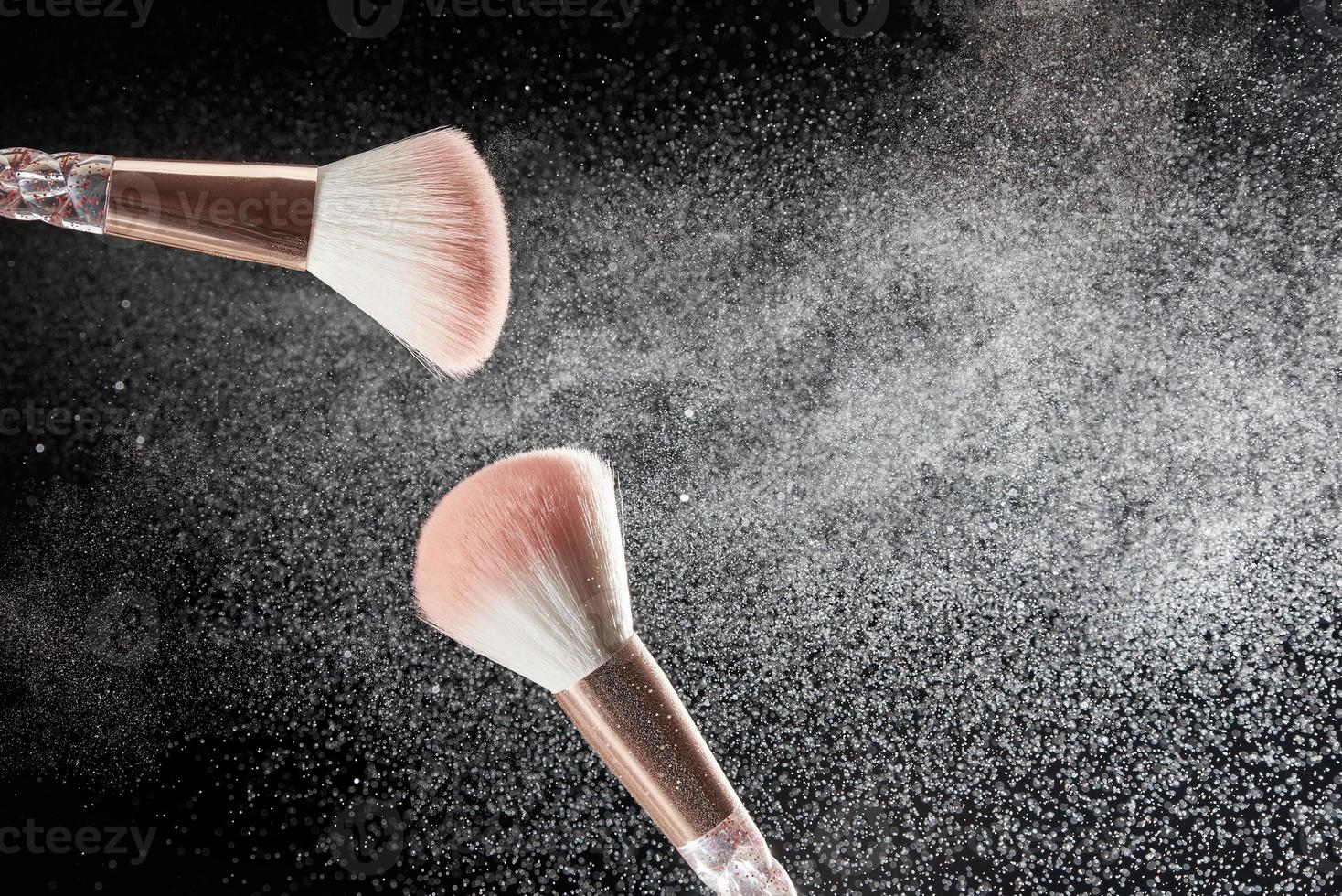 Make-up brushes with powder on it and heap of powder on black background. Photo with copy space.