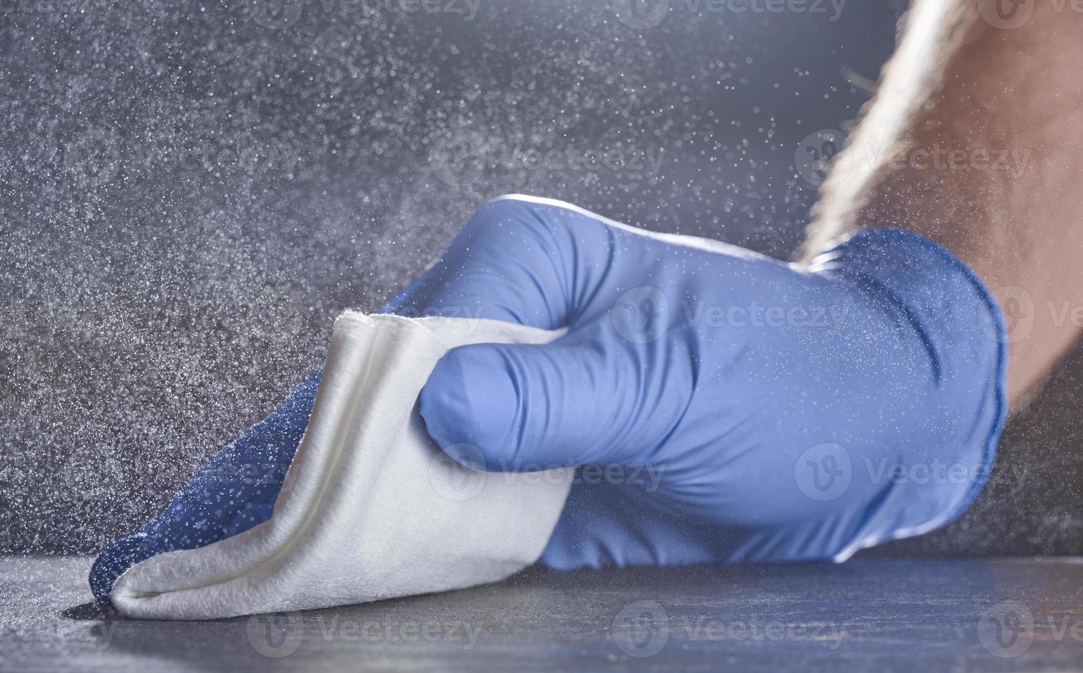 una mano en un guante médico limpia la mesa. fondo gris con salpicaduras de desinfectante. foto