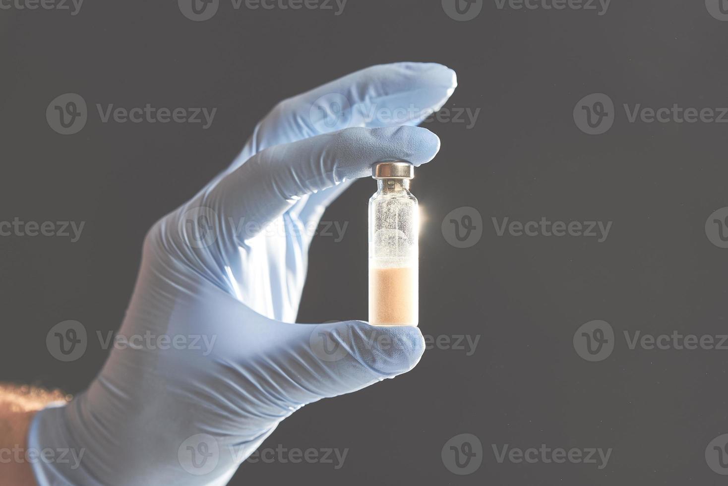 A doctor holds a vial full of blue liquid with his latex gloves on. Isolated on gray. photo