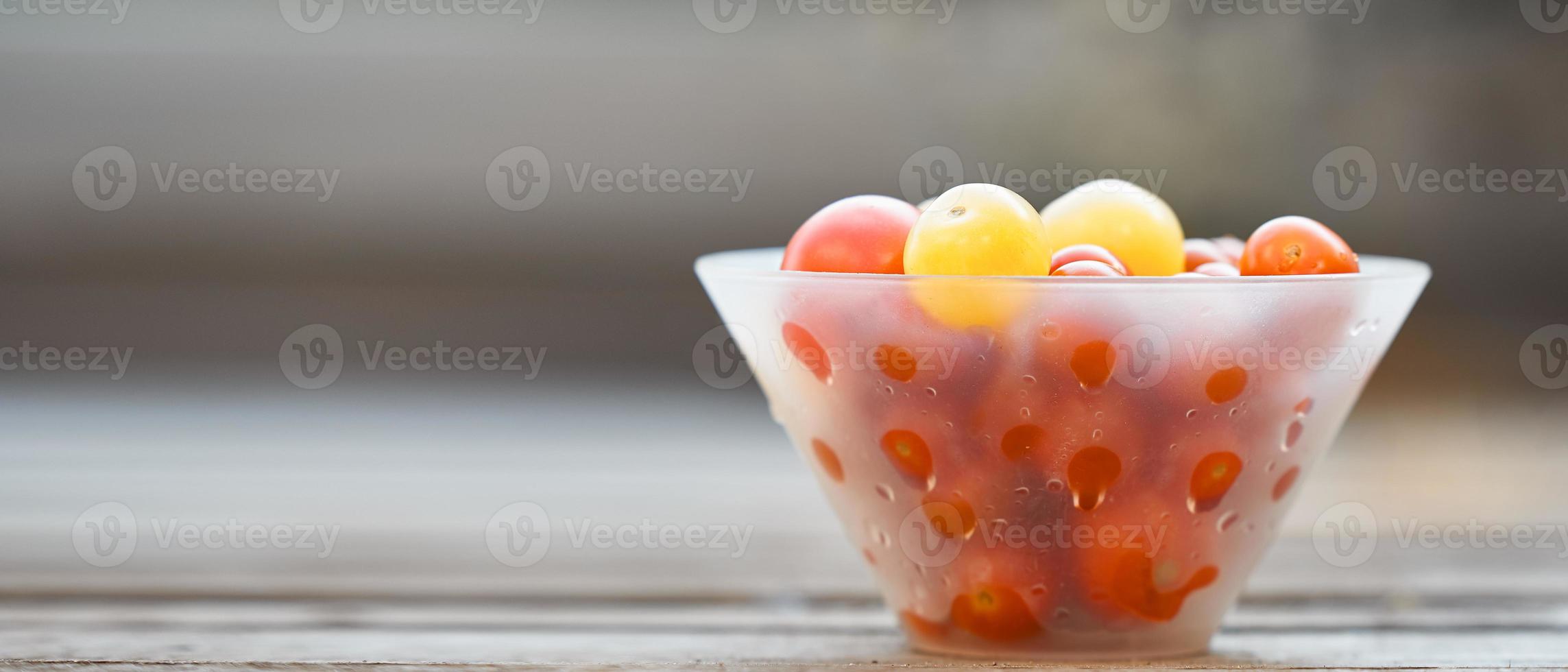 Transparent white bowl with small colorful cherry tomatoes on wooden background in a blur. photo