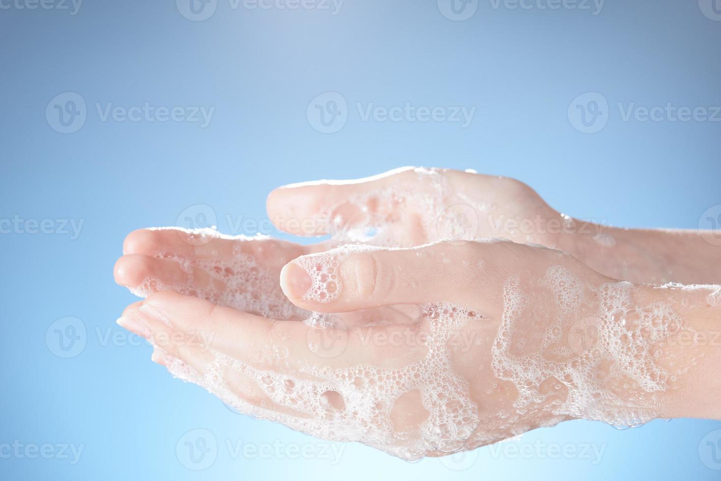 Woman's hands in soapsuds, on blue background close-up. photo
