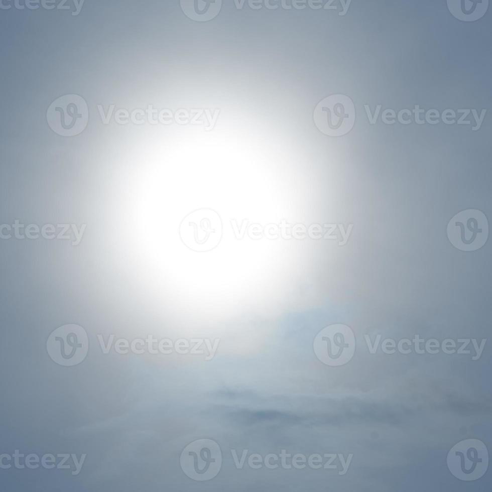 A large solar disk shines through the clouds. Blue and white background. photo