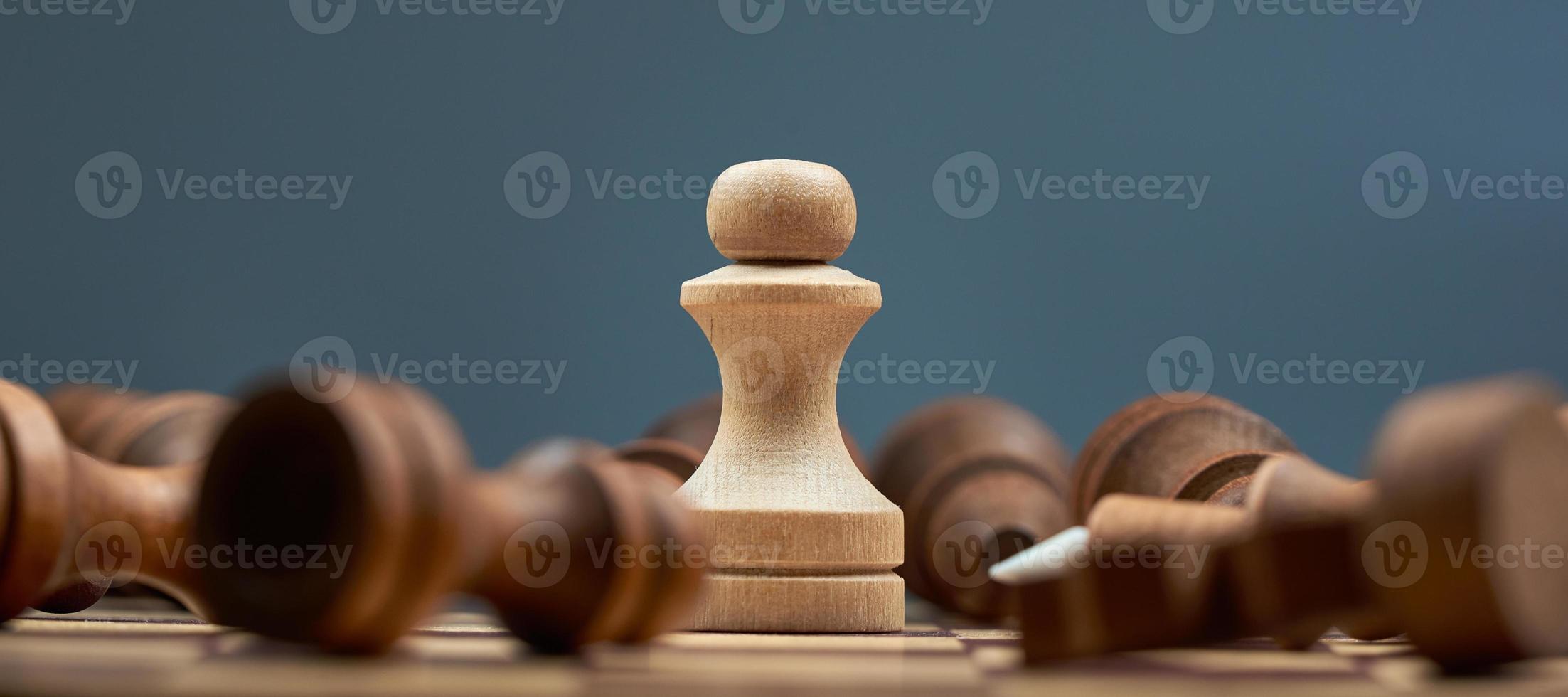 White pawn on the blur background of lying black chess pieces. The concept of one against all. photo