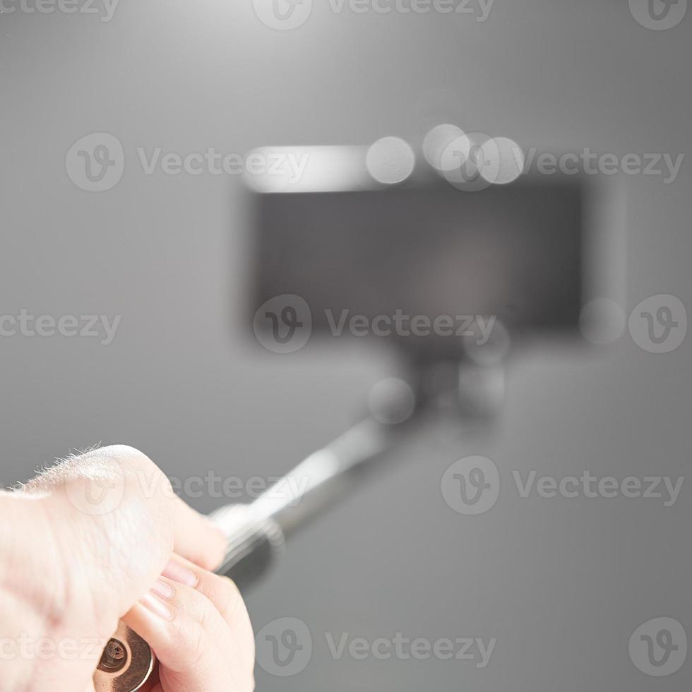 Taking selfie - hand hold monopod with mobile phone on grey background in blur. photo