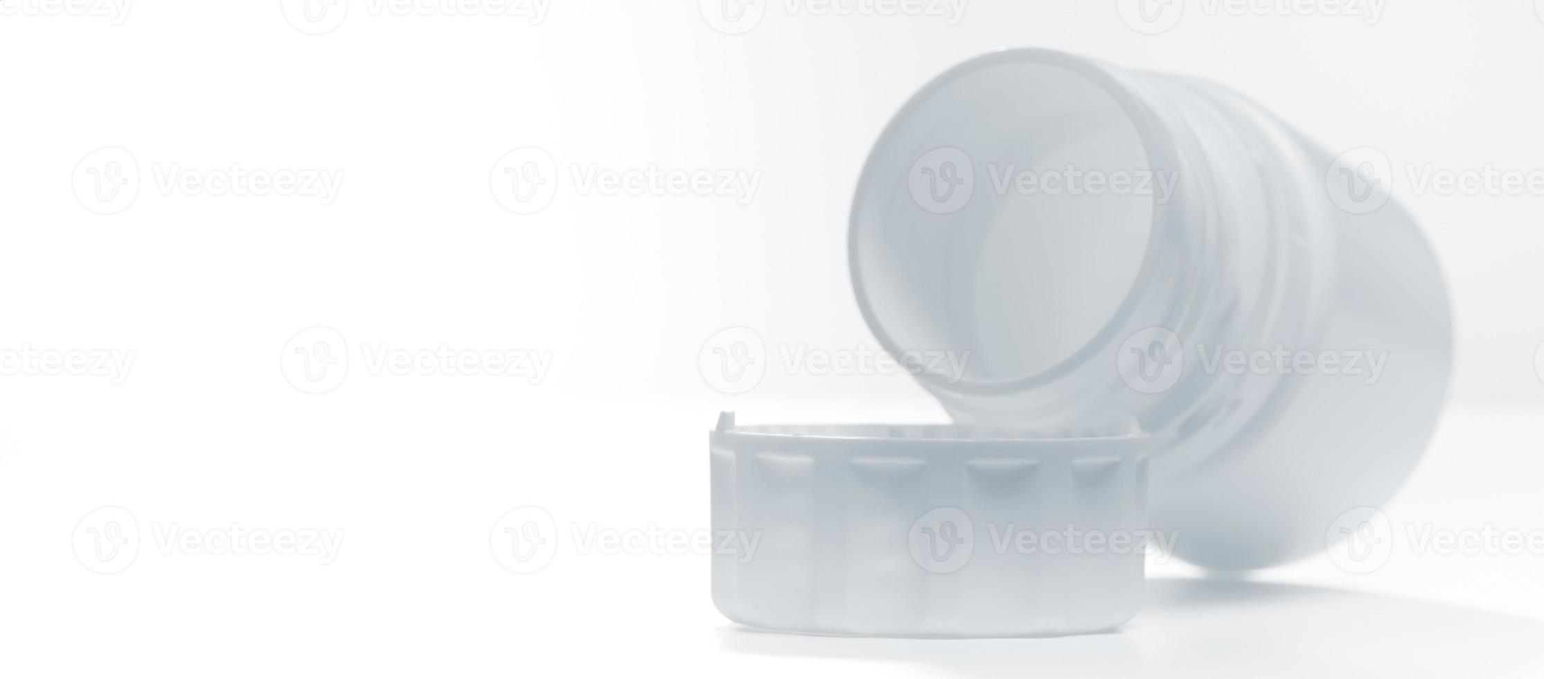White plastic bottlefor tablets lying near lid horizontally isolated on white background. Photo with copy space.