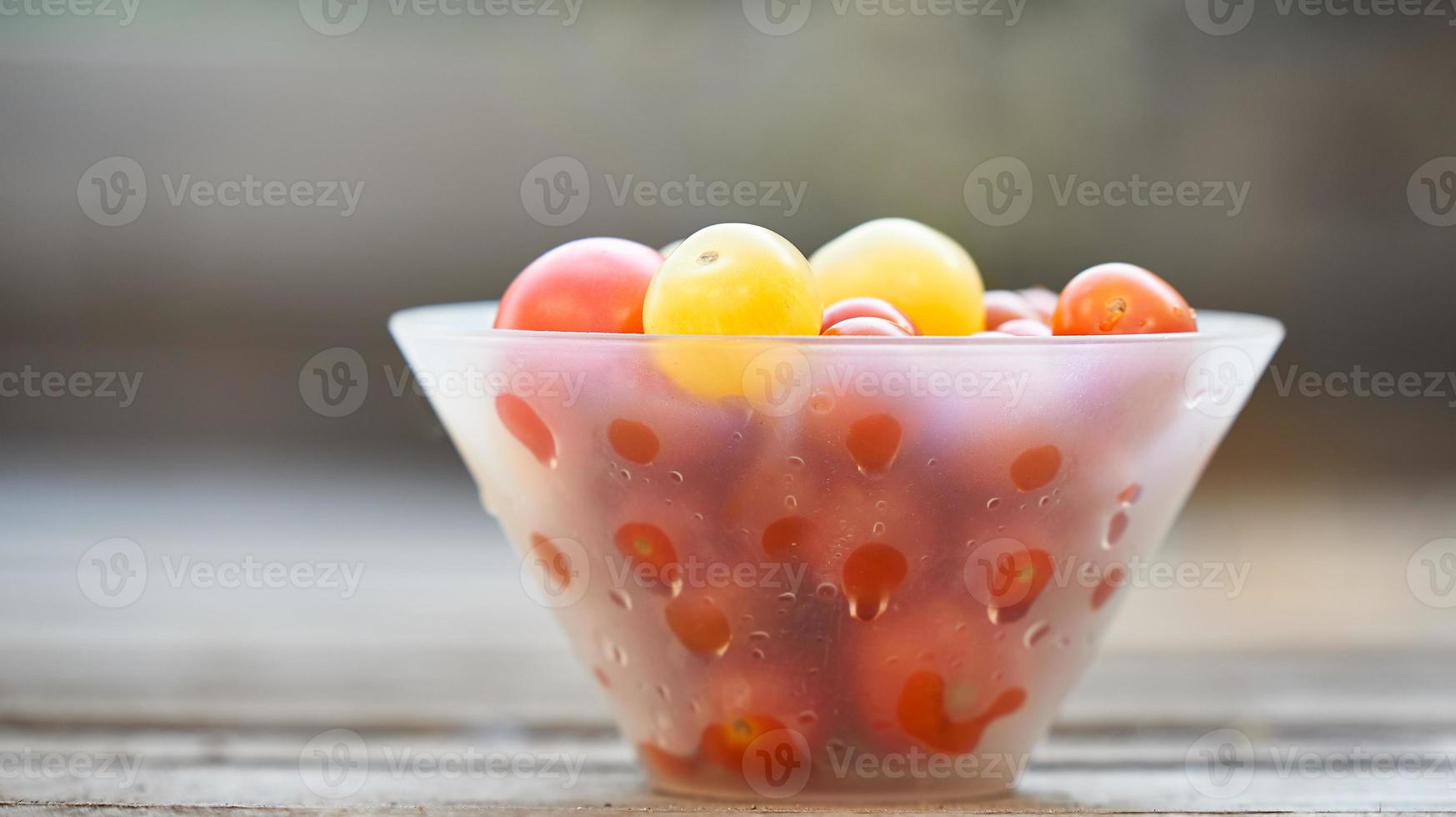 Different sorts of tomatoes served on a white bowl on a wooden background in a blur. photo