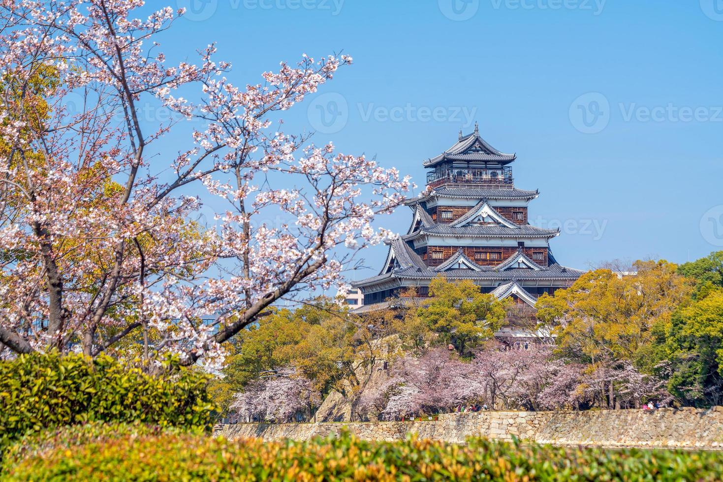 castillo de hiroshima durante el día de la temporada de los cerezos en flor en japón foto