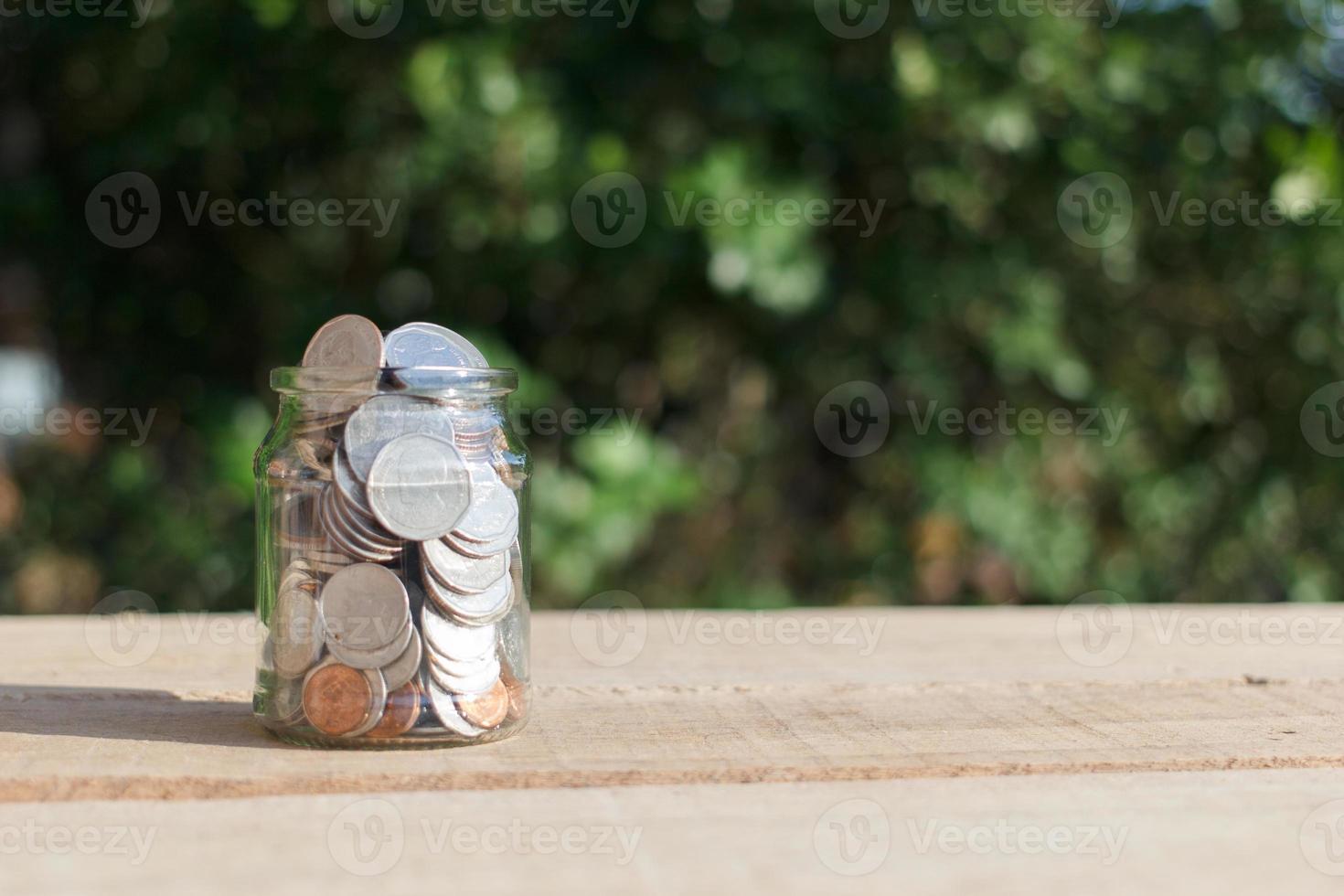 monedas en un frasco transparente colocado sobre tablones de madera al aire libre en el jardín, concepto de ahorro de inversión. copie el espacio. foto