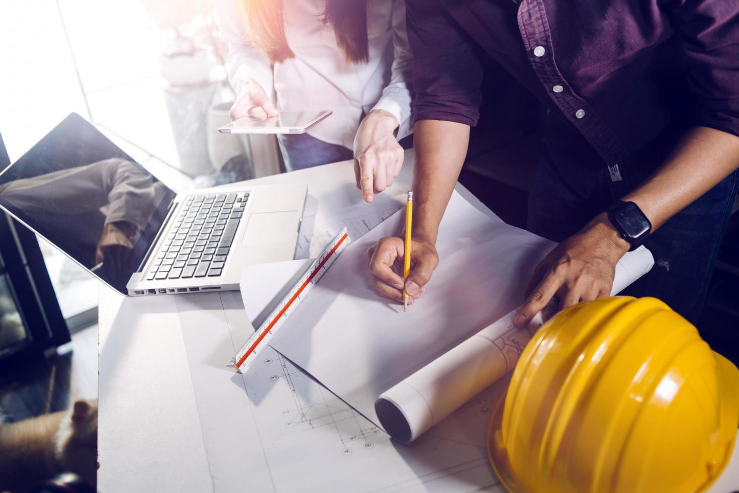 Dos colegas discutiendo el trabajo de datos y una tableta, un portátil con un proyecto arquitectónico en el sitio de construcción en un escritorio en la oficina foto