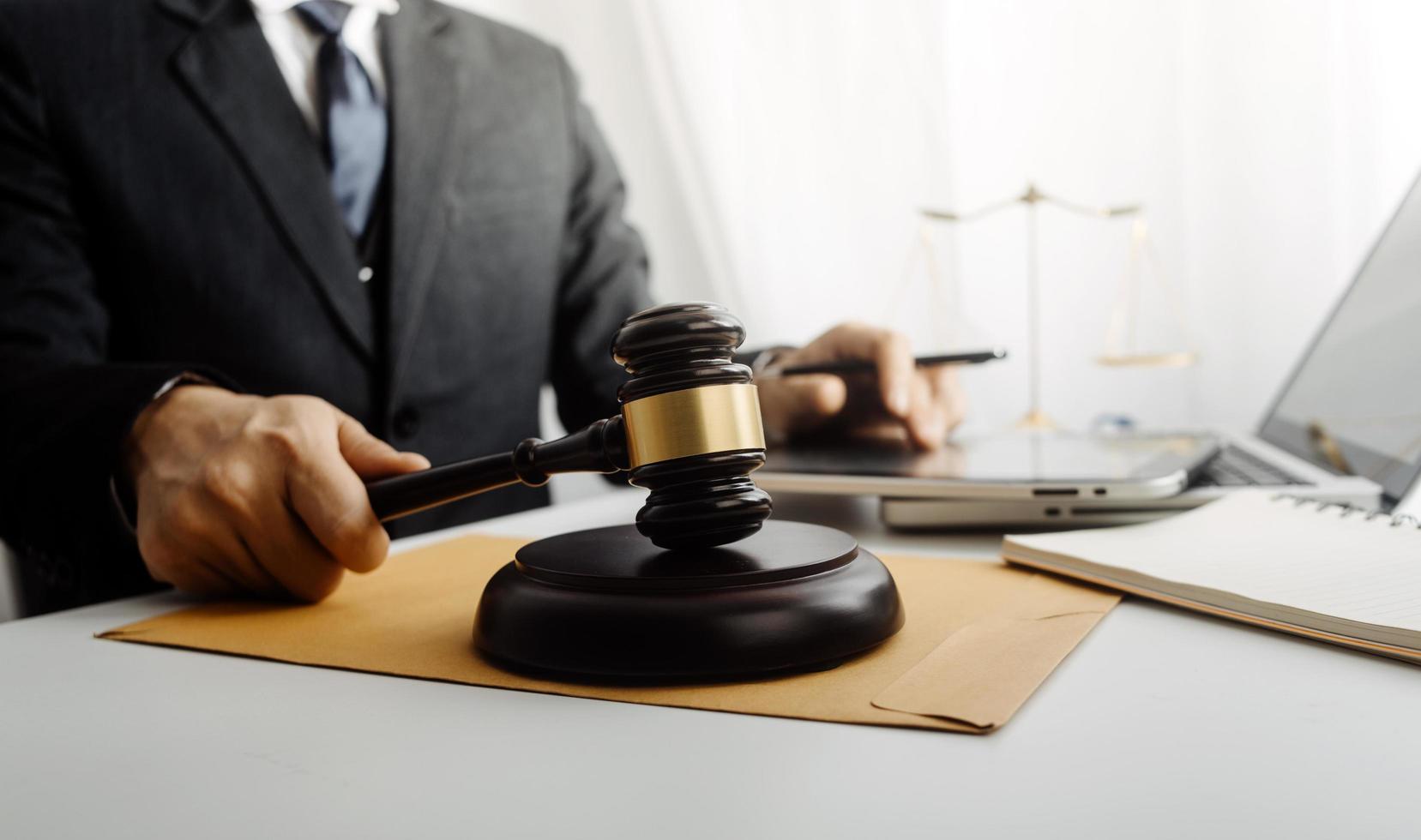 Justice and law concept.Male judge in a courtroom with the gavel, working with, computer and docking keyboard, eyeglasses, on table in morning light photo