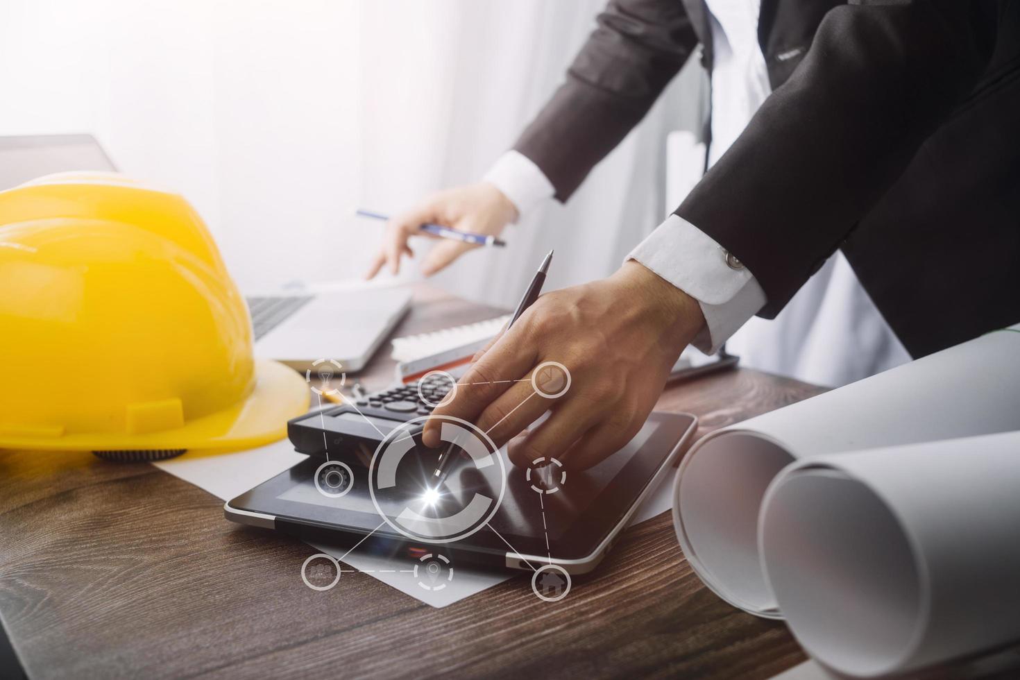 Dos colegas discutiendo el trabajo de datos y una tableta, un portátil con un proyecto arquitectónico en el sitio de construcción en un escritorio en la oficina foto