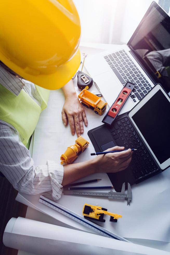 Dos colegas discutiendo el trabajo de datos y una tableta, un portátil con un proyecto arquitectónico en el sitio de construcción en un escritorio en la oficina foto