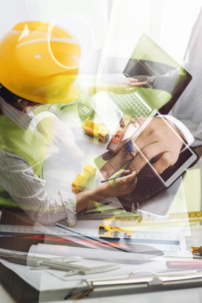 Two colleagues discussing data working and tablet, laptop with on on architectural project at construction site at desk in office photo