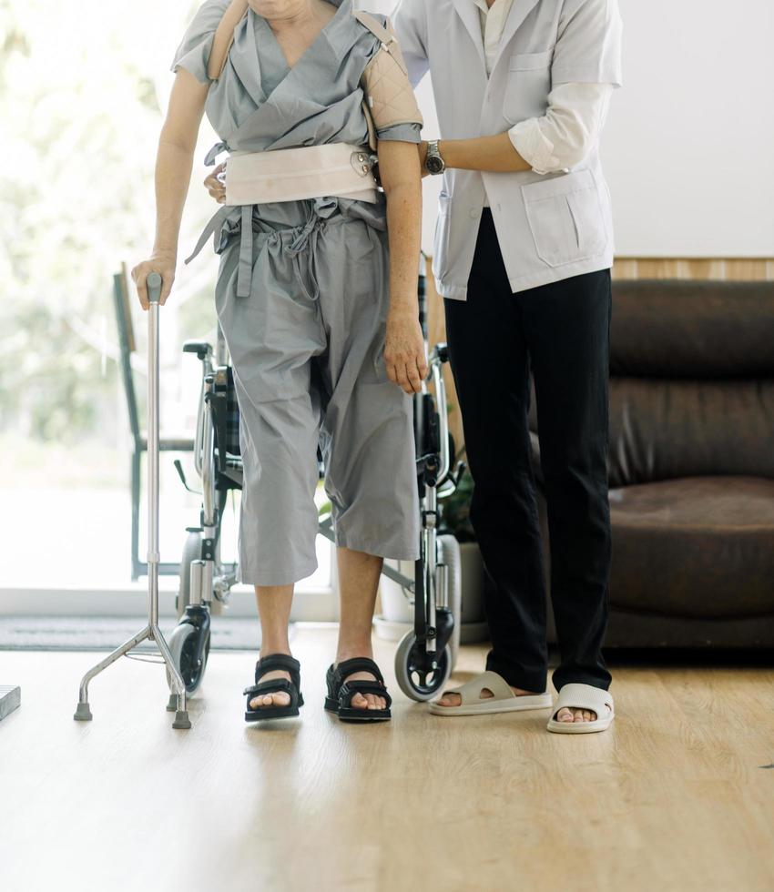 joven fisioterapeuta asiático que trabaja con un anciano usando un andador en el pasillo de un hogar de ancianos foto