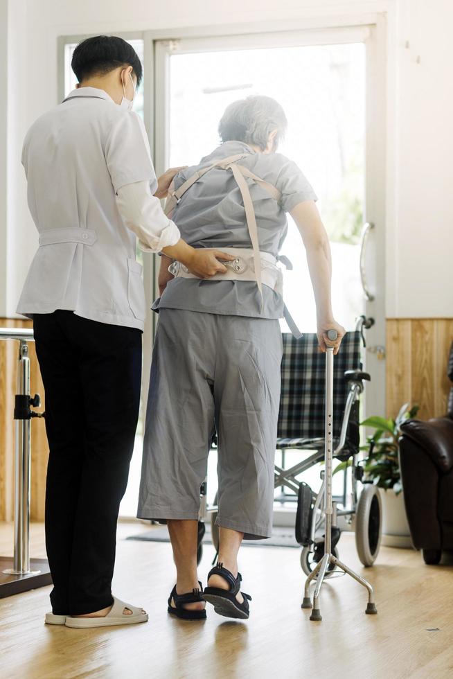 joven fisioterapeuta asiático que trabaja con un anciano usando un andador en el pasillo de un hogar de ancianos foto