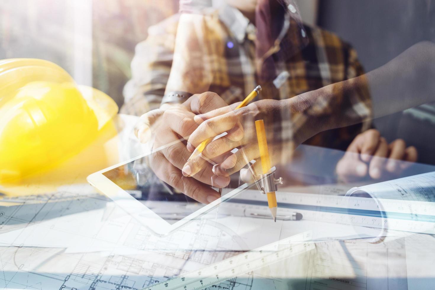 Two colleagues discussing data working and tablet, laptop with on on architectural project at construction site at desk in office photo