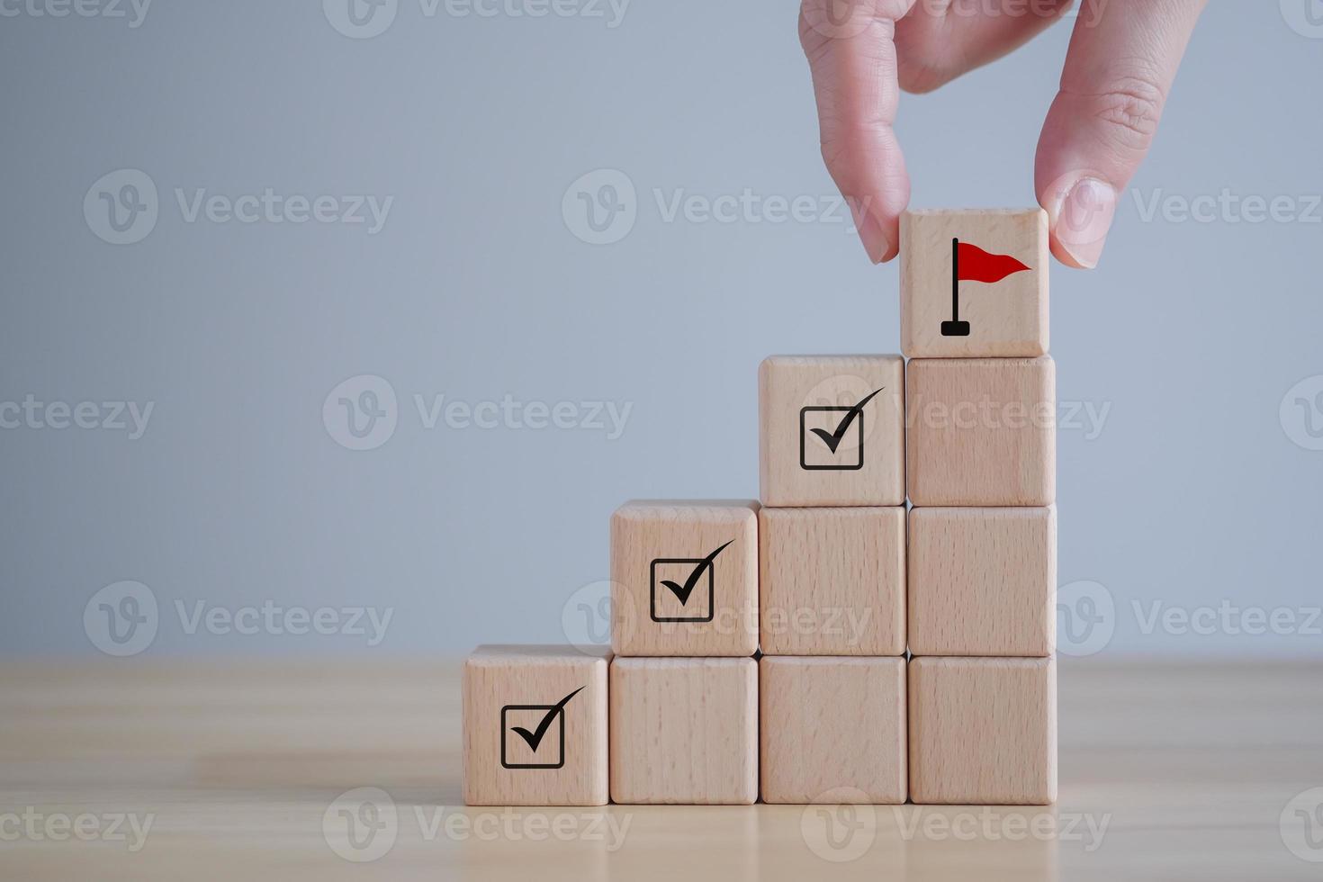 Checklist Survey and assessment. quality Control. Goals achievement and business success. Hand Holding wooden block with red flag icon and check mark on cube ladder. photo