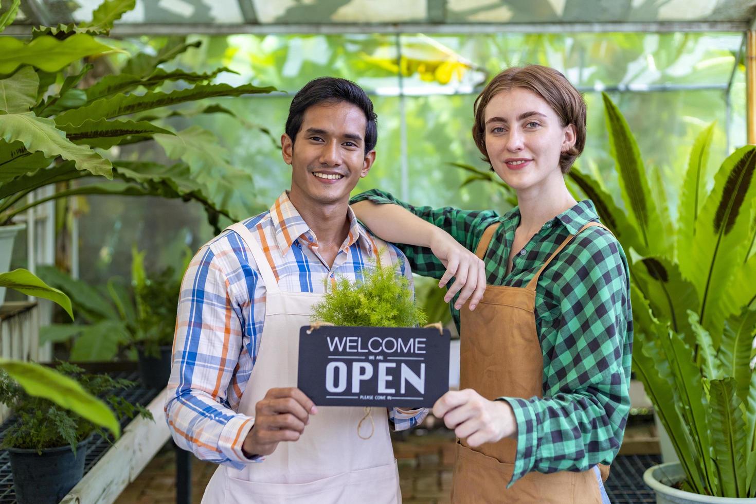 Team of diversity garden worker holding opening sign to welcome customer to their tropical nursery plant center full of exotic fern species photo