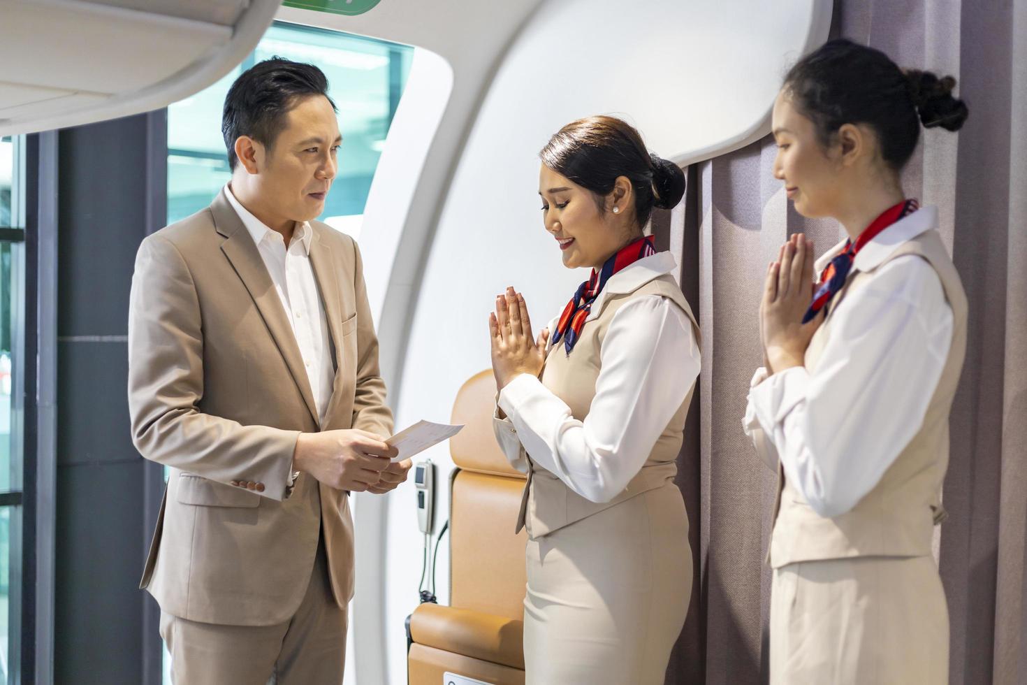 Flight attendant is welcoming and checking passenger boarding pass in business class and show the way to his seat for airplane flight and airline transportation photo