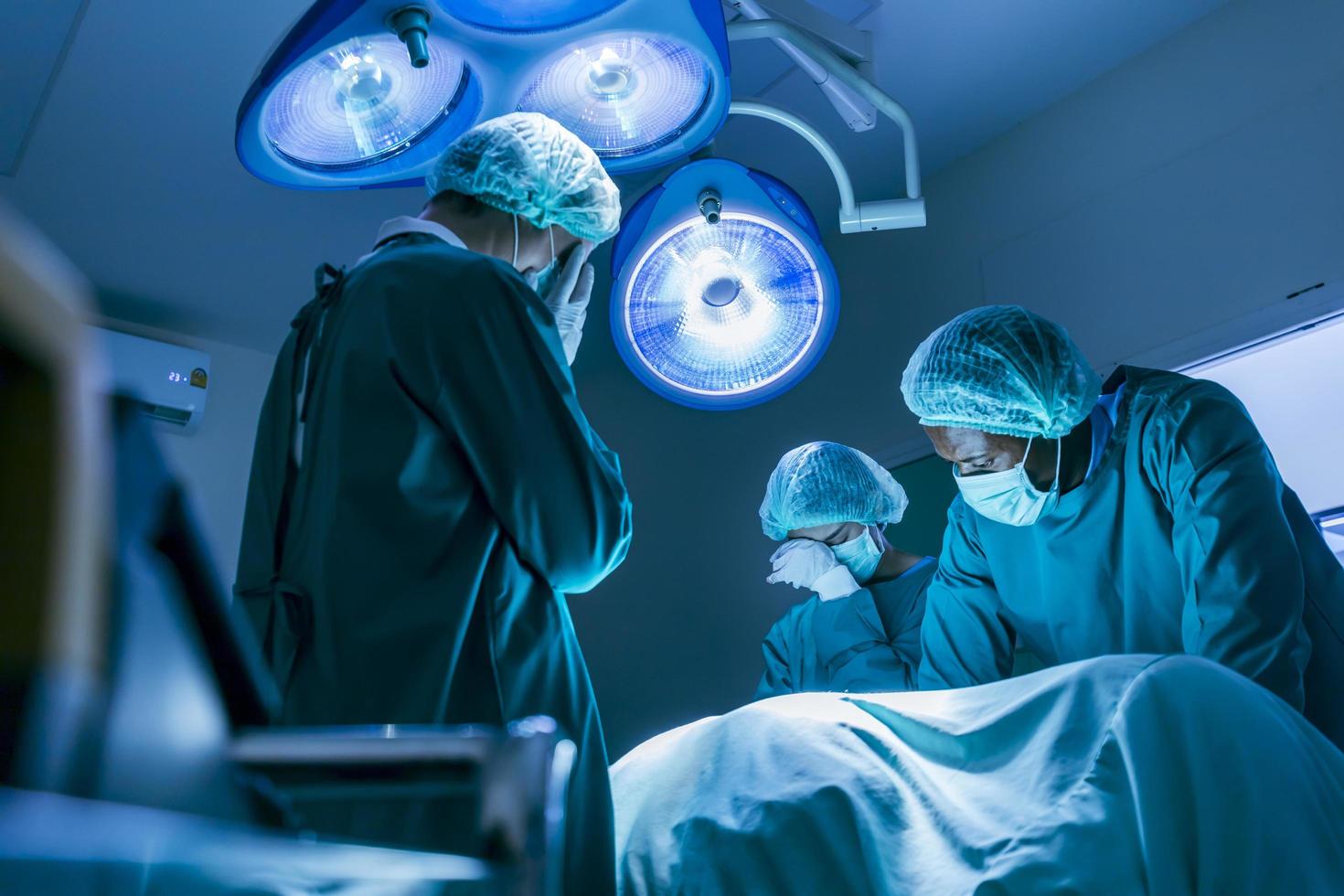 Team of surgeon doctors are crying and mourning over the patient's dead body from incurable disease after hours of operation failure inside emergency surgical room photo